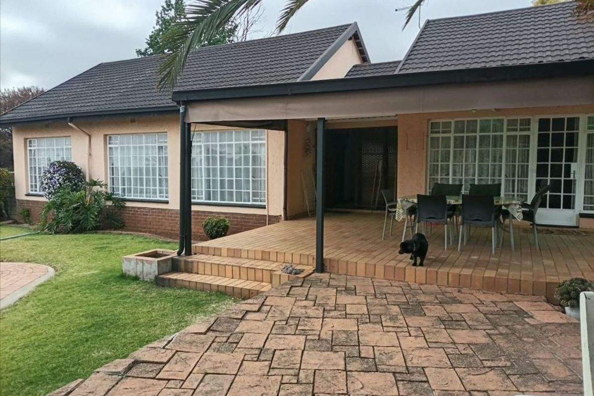Rear view of the house featuring a tiled patio, paved courtyard area, and a well-maintained lawn under a covered outdoor space.