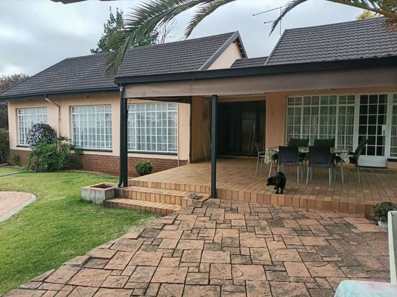 Rear view of the house featuring a tiled patio, paved courtyard area, and a well-maintained lawn under a covered outdoor space.