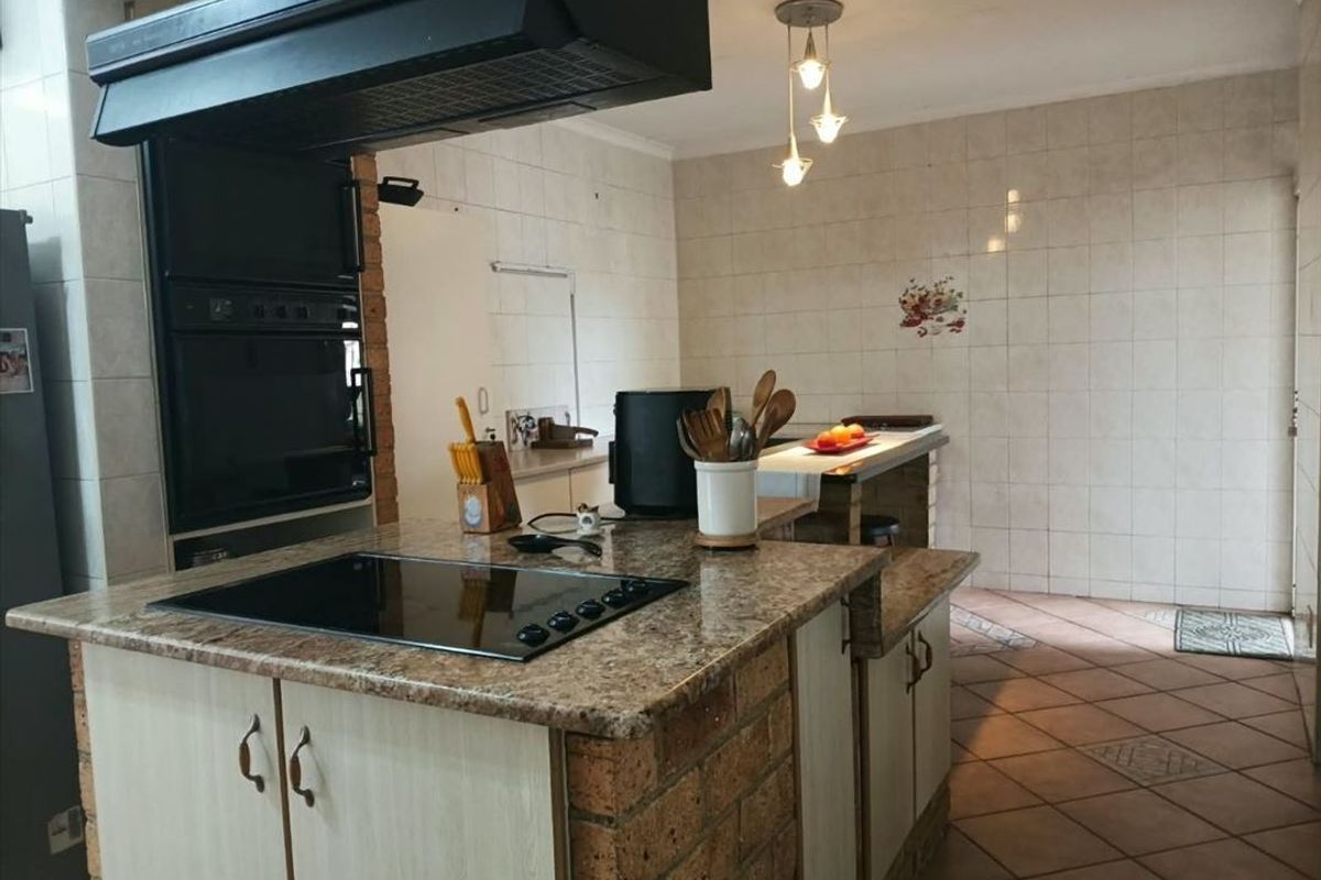 A functional kitchen featuring a brick-based island with a granite countertop, built-in oven, extractor fan, and tiled finishes throughout.
