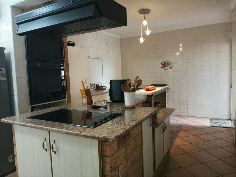 A functional kitchen featuring a brick-based island with a granite countertop, built-in oven, extractor fan, and tiled finishes throughout.