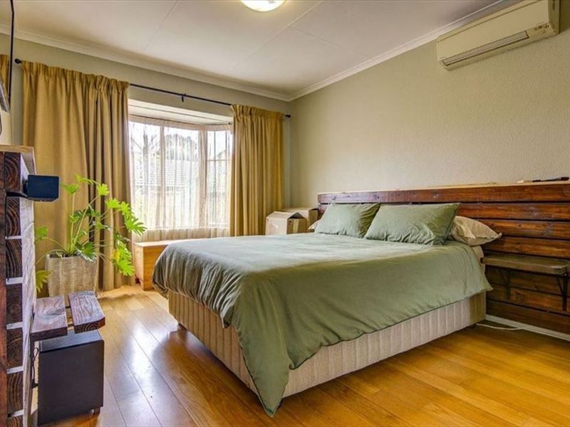 A well-proportioned bedroom featuring hardwood flooring, a bay window for natural light, and a wall-mounted air conditioning unit for climate control.