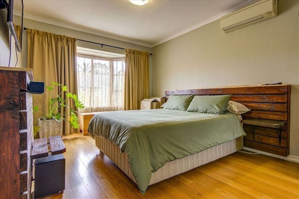 A well-proportioned bedroom featuring hardwood flooring, a bay window for natural light, and a wall-mounted air conditioning unit for climate control.