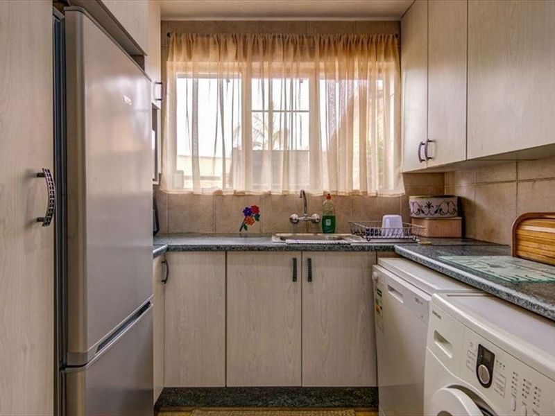 A functional scullery featuring laminate cabinetry, granite countertops, a stainless steel sink, and tiled backsplash, providing additional prep and utility space.