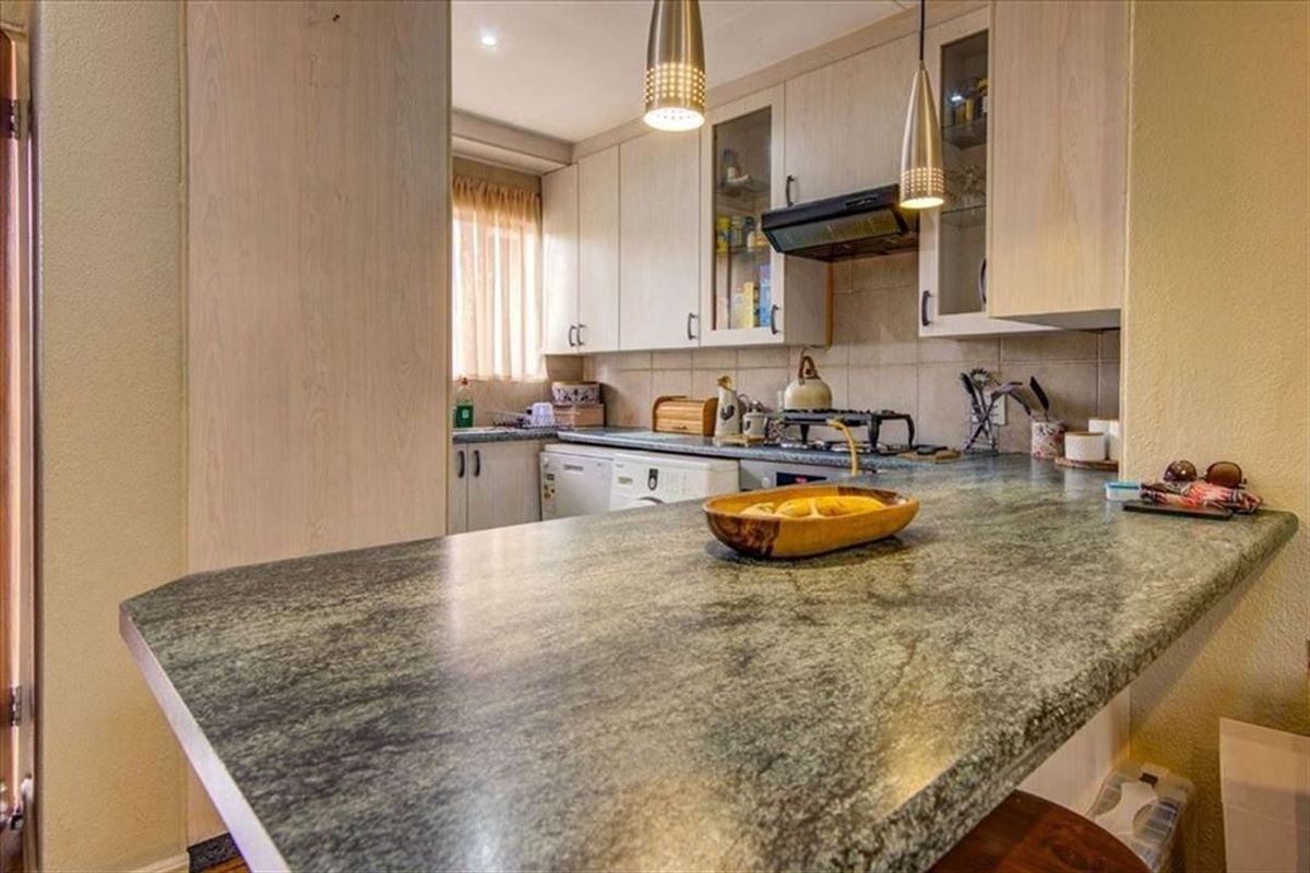 Functional kitchen featuring laminate cabinetry, stone-look countertops, a built-in gas hob with extractor fan, and a breakfast bar area.