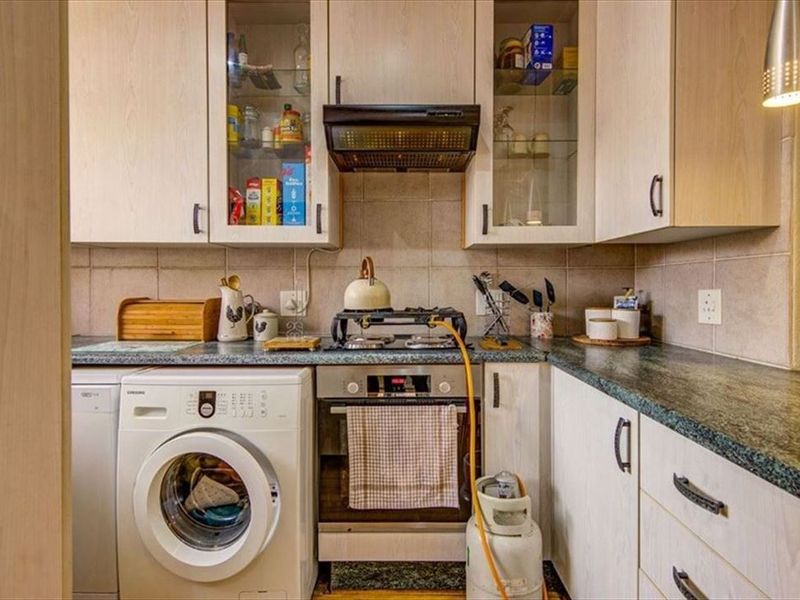 Compact kitchen featuring light wood-finish cabinetry, laminate countertops, built-in oven, gas hob with extractor fan, and integrated space for a washing machine.