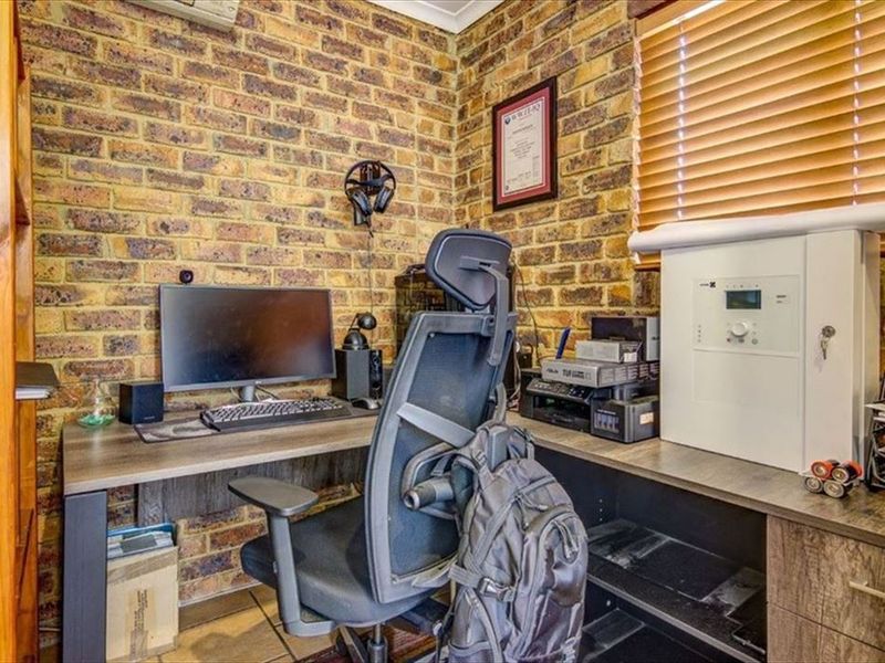 A functional home office featuring exposed brick walls, tiled flooring, and venetian blinds, providing a rustic yet practical workspace.