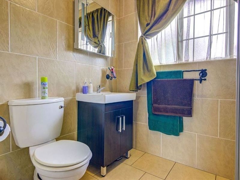 A functional bathroom featuring a vanity cabinet with basin, toilet, and tiled finishes throughout, complemented by a window for natural light.