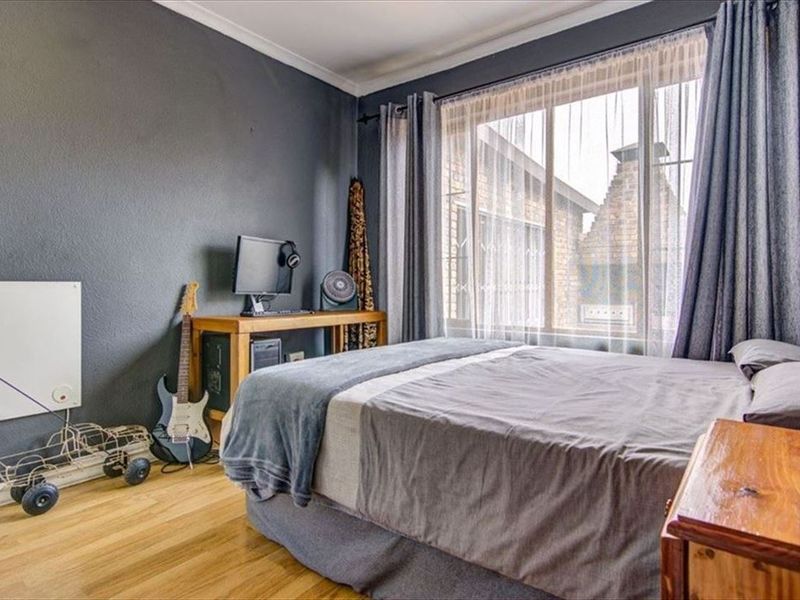 A bedroom featuring laminate flooring, a large window with natural light, and a wall-mounted heater.
