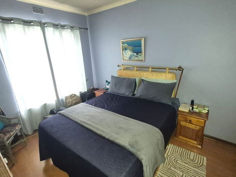 A standard bedroom featuring light blue walls, laminate flooring, and a large window with curtains.