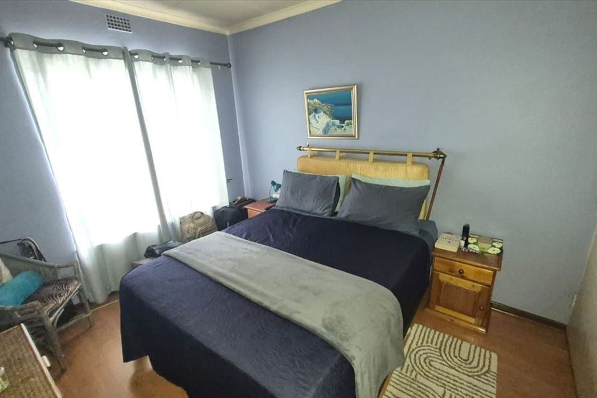 A standard bedroom featuring light blue walls, laminate flooring, and a large window with curtains.