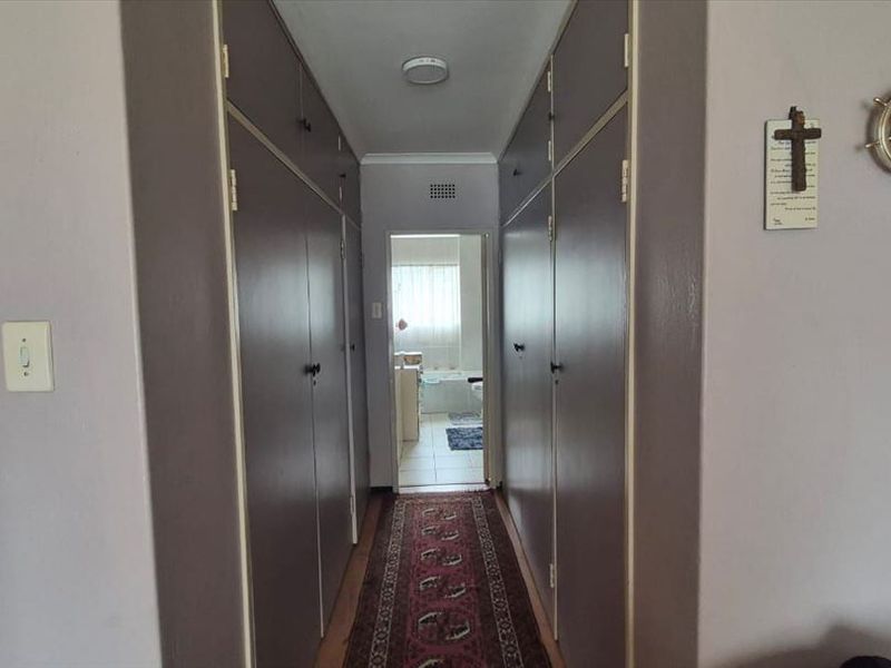 A functional hallway featuring extensive built-in storage cupboards along both walls, leading towards a bathroom area.