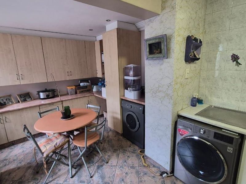 A functional kitchen featuring laminate cabinetry, tiled backsplash, and integrated laundry space, offering a practical layout with potential for modern cosmetic updates.