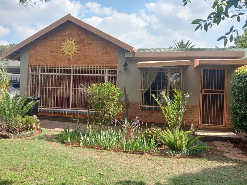 Front elevation of a residential house featuring brick accents, security bars on windows, a security gate, and a landscaped front garden.