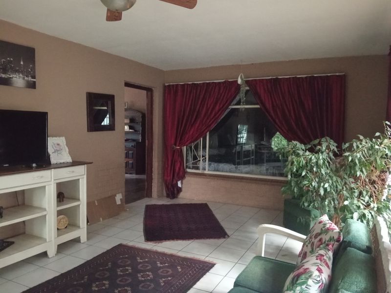 A living room featuring tiled flooring, a ceiling fan, and a large window with security bars, offering a functional space for relaxation.
