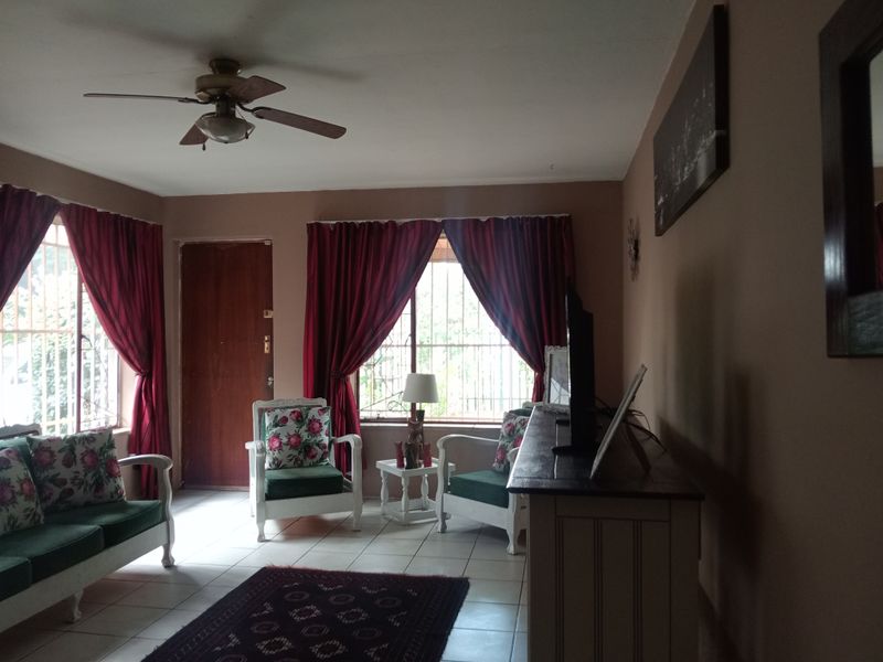 A living room featuring tiled flooring, a ceiling fan, and security bars on the windows, providing a functional and secure living space.