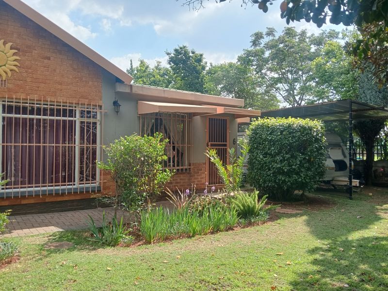 Front elevation of a residential house featuring brick cladding, security bars, a paved walkway, and an adjacent carport structure.