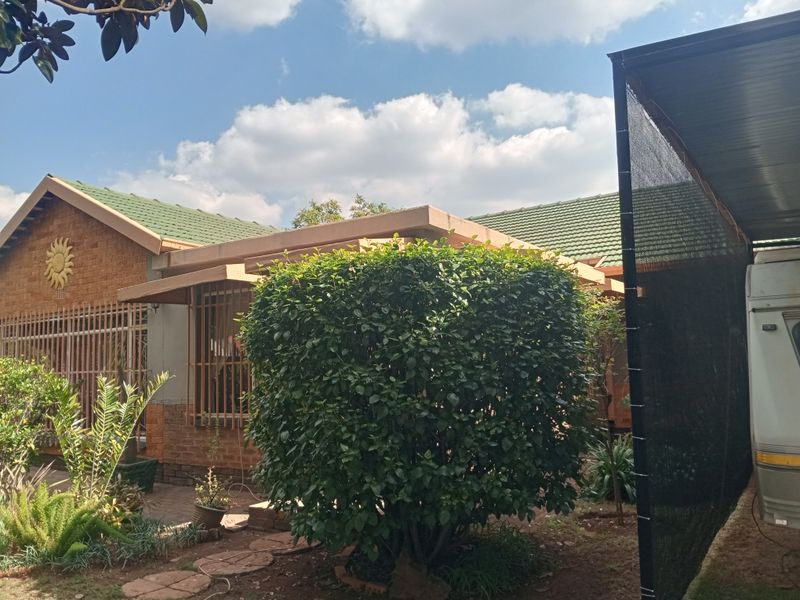 Front view of a facebrick house featuring a green tiled roof, security bars on windows, and an adjacent carport structure.