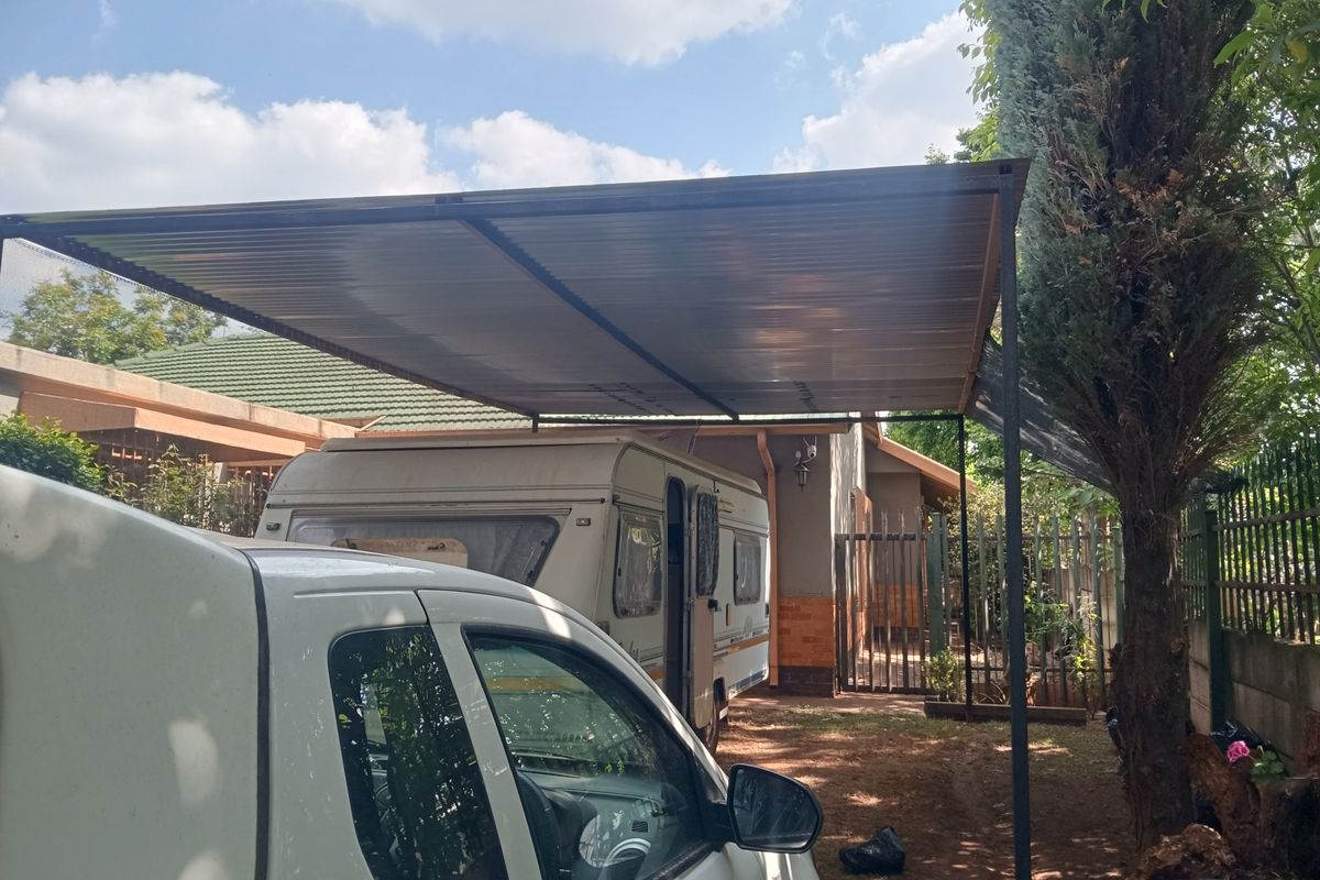 A functional outdoor carport structure providing covered parking space, featuring a metal roof and steel support posts.