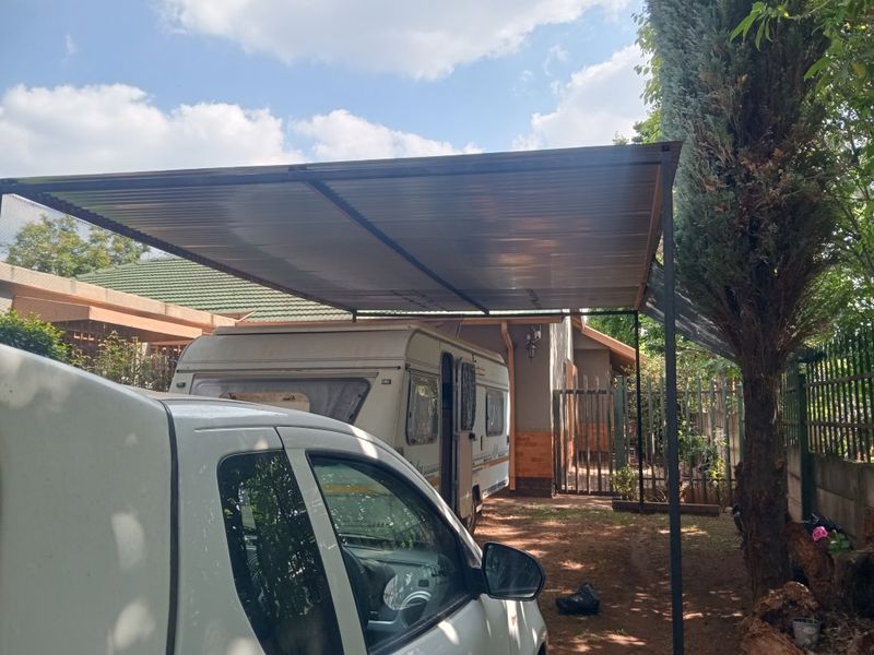 A functional outdoor carport structure providing covered parking space, featuring a metal roof and steel support posts.
