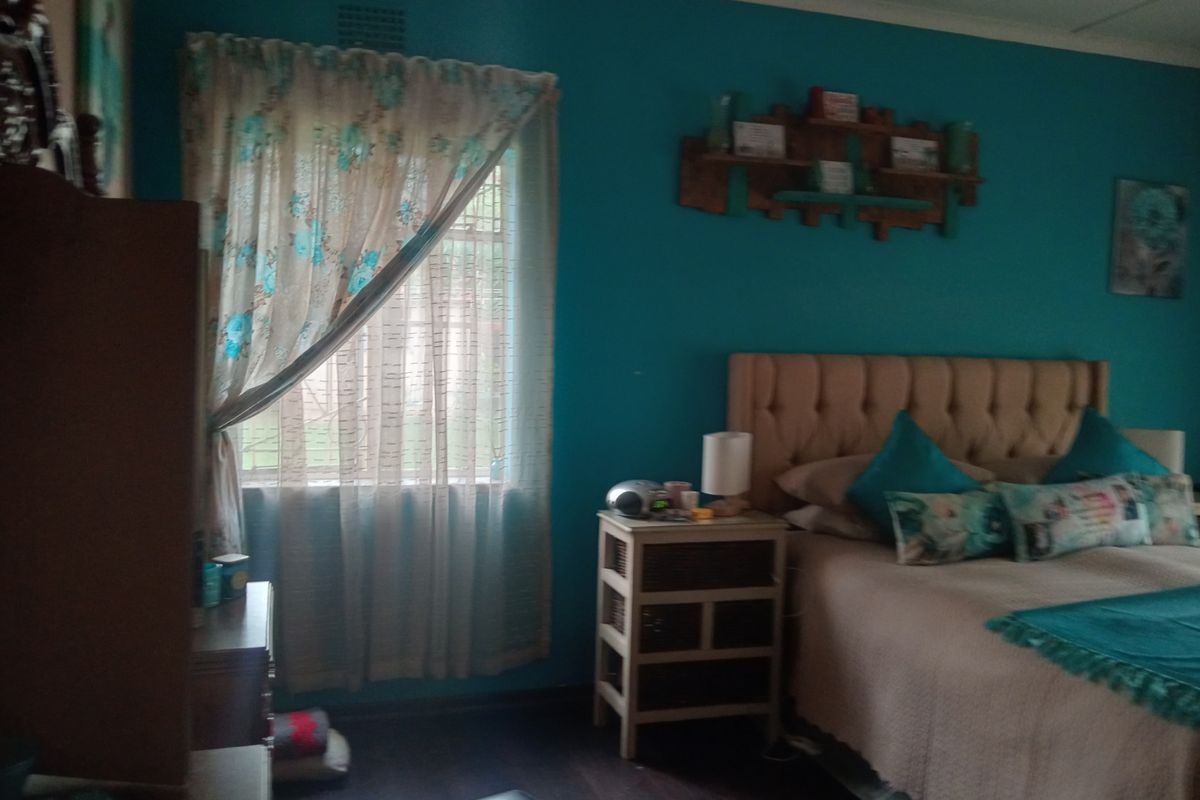 A bedroom featuring dark wood-look flooring, a ceiling fan, and a window with curtains.