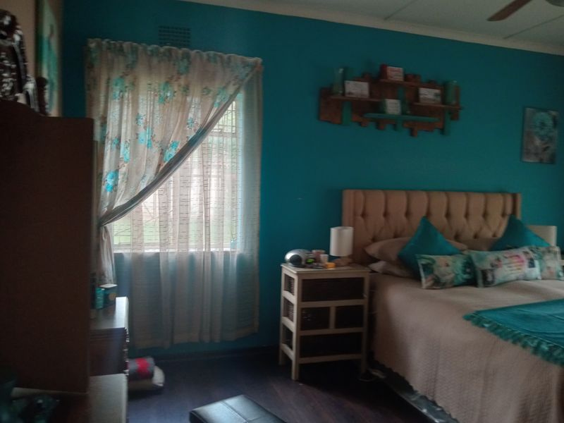 A bedroom featuring dark wood-look flooring, a ceiling fan, and a window with curtains.