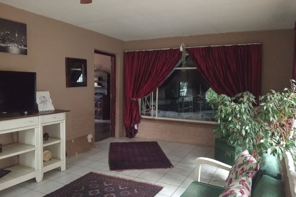 A living room featuring tiled flooring, a ceiling fan, and a large window with security bars, offering a functional space for relaxation.