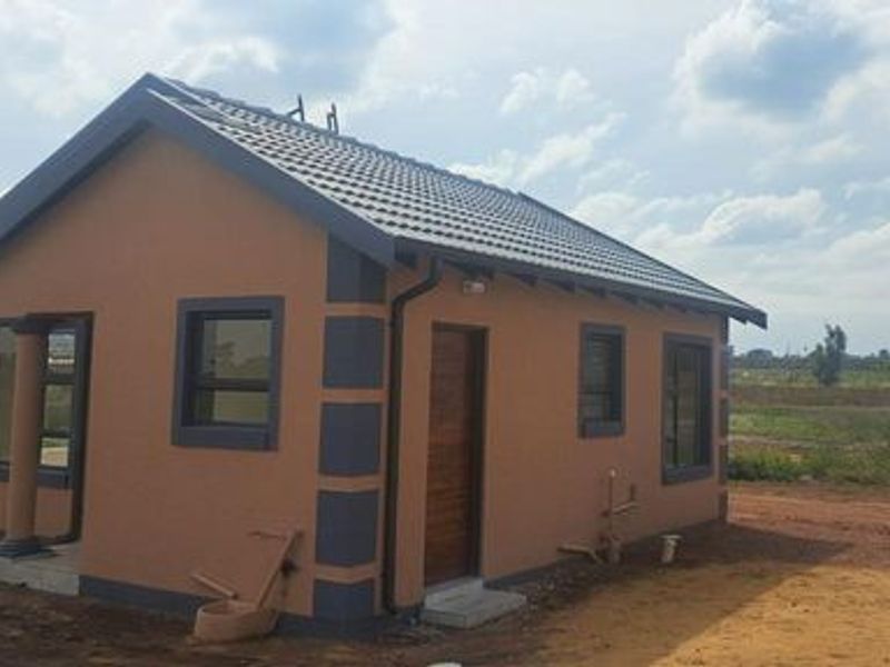 A newly constructed single-story house featuring a tiled roof, modern exterior paint finish, and aluminium window frames, set on an undeveloped plot.
