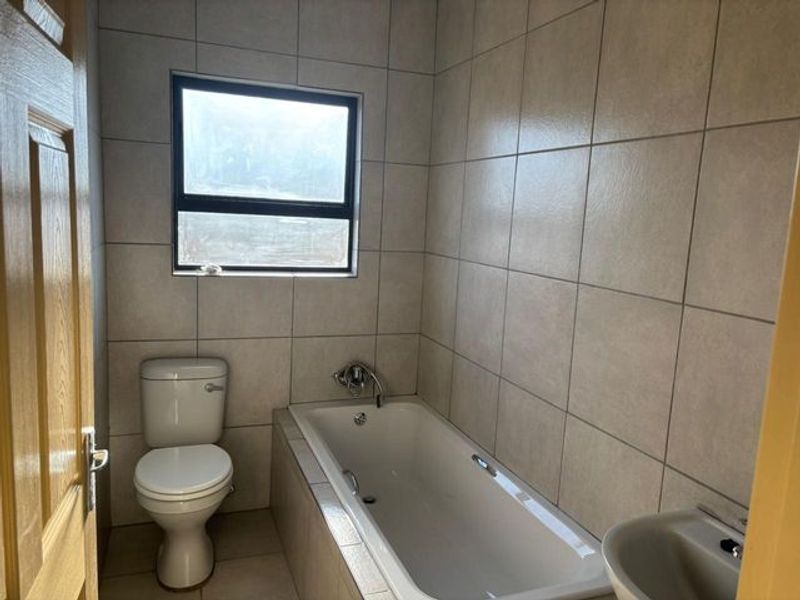 A functional bathroom featuring a bathtub, toilet, and basin with neutral wall and floor tiling.