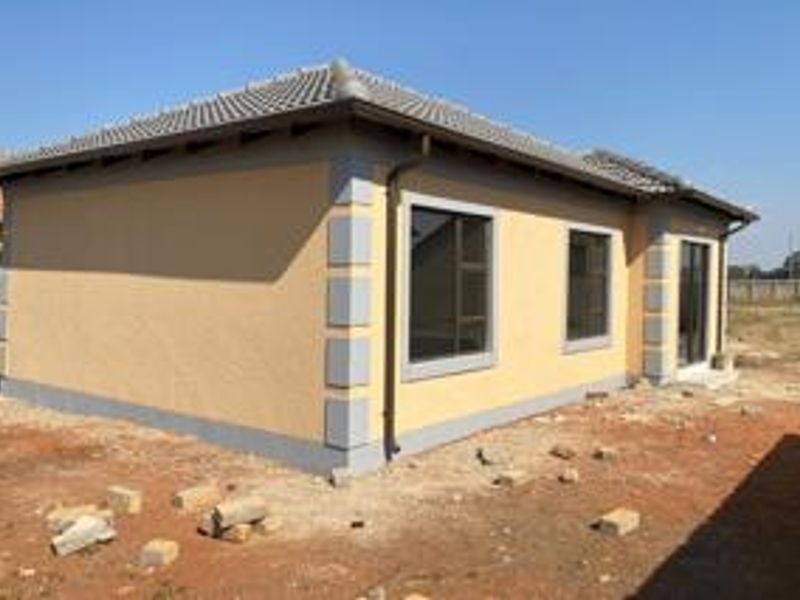 A rear view of a modern single-story house featuring a tiled roof, plastered walls with corner detailing, and aluminium window frames.