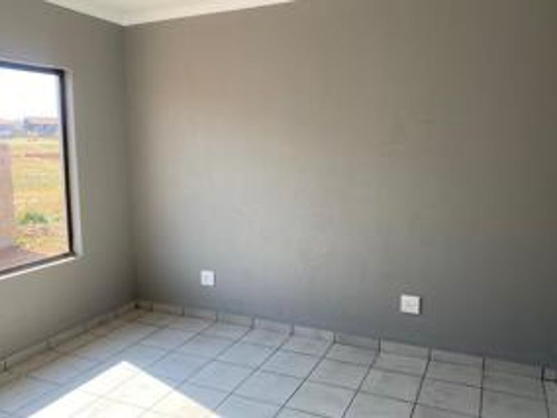 A clean, empty bedroom featuring neutral grey walls, tiled flooring, and a large window providing natural light.