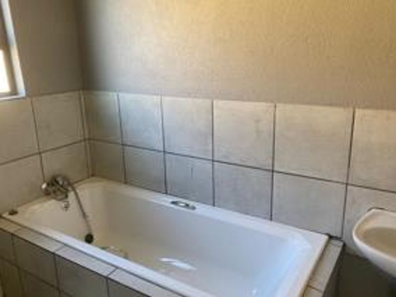 A functional bathroom featuring a built-in bathtub with shower mixer, tiled splashbacks, and a pedestal basin.