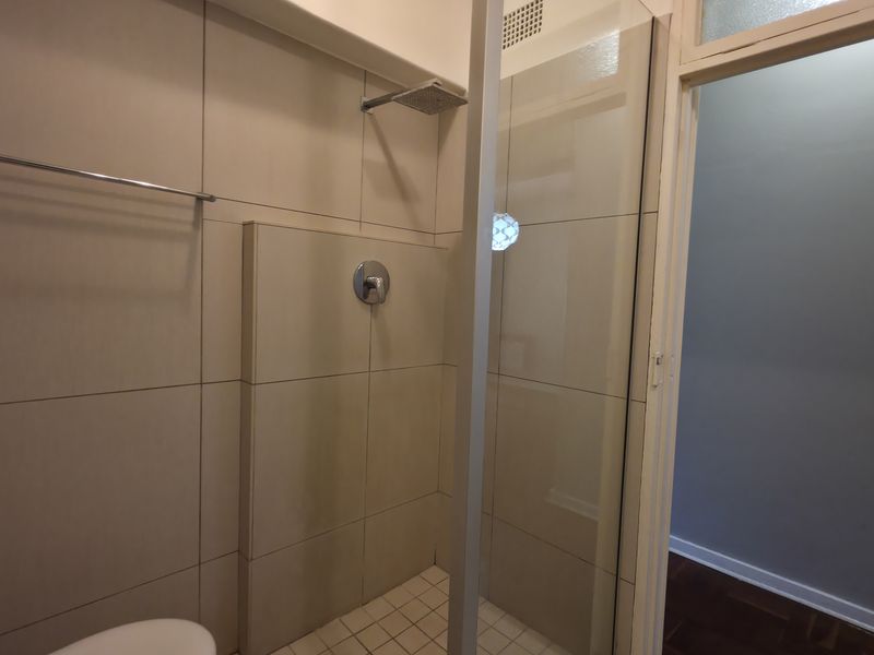 A clean, modern bathroom featuring a walk-in shower with a glass screen, neutral wall tiling, and a fixed shower head.