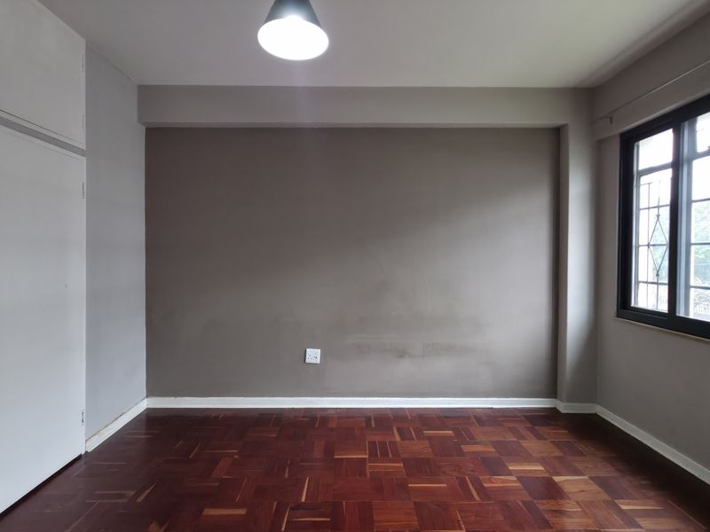 An empty bedroom featuring classic parquet flooring, built-in cupboards, and large windows with security bars, offering a neutral canvas for personalization.