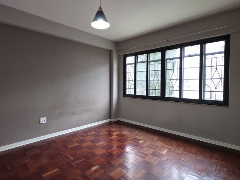 An empty bedroom featuring polished parquet flooring, large black-framed windows with security bars, and neutral wall tones, offering a clean canvas for personalization.