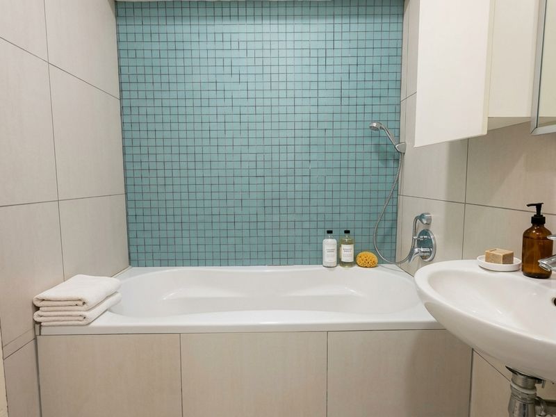 A clean bathroom featuring a bathtub with a handheld shower attachment, a mosaic tile feature wall, and a pedestal sink.