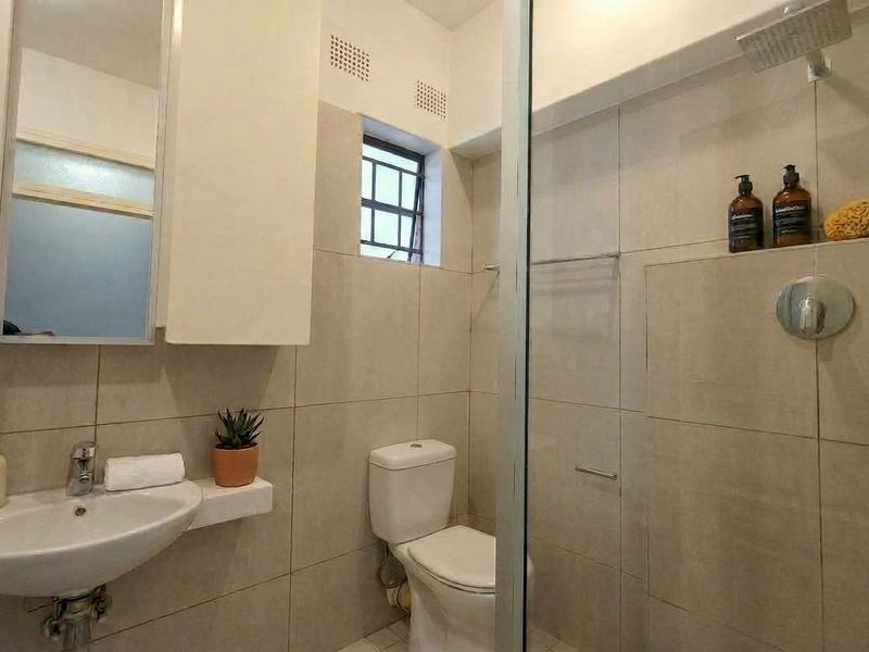 A modern bathroom featuring a wall-mounted basin, a toilet, and a glass-enclosed shower with a rain shower head and neutral wall tiling.