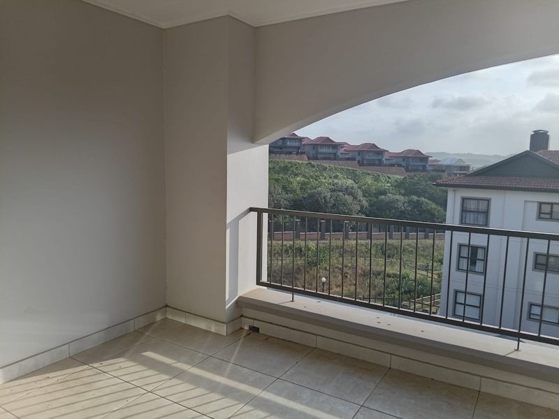 A covered balcony featuring tiled flooring and a metal balustrade, offering an open view of the surrounding residential estate.