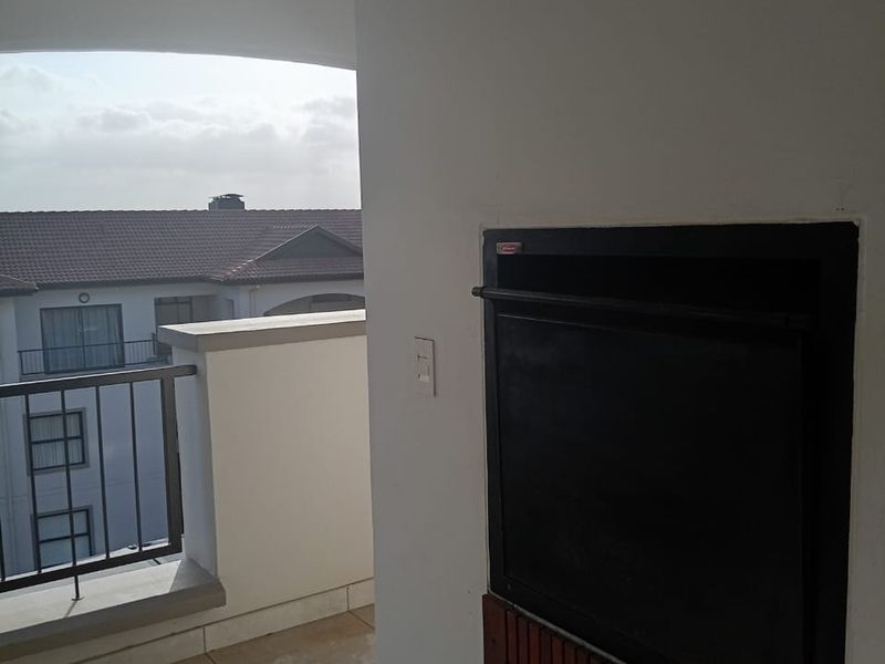 A covered balcony featuring tiled flooring, a built-in braai, and a metal balustrade with views of the surrounding complex.