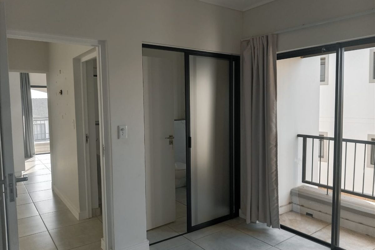 An empty bedroom featuring tiled flooring, a sliding glass door leading to a private balcony, and an en-suite bathroom entrance.