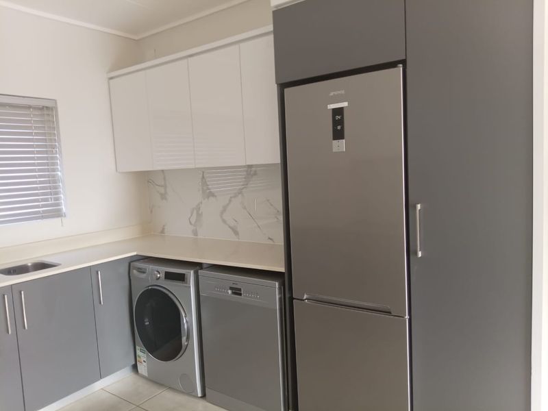 Modern kitchen featuring sleek grey and white cabinetry, marble-look splashback, stone countertops, and integrated stainless steel appliances.