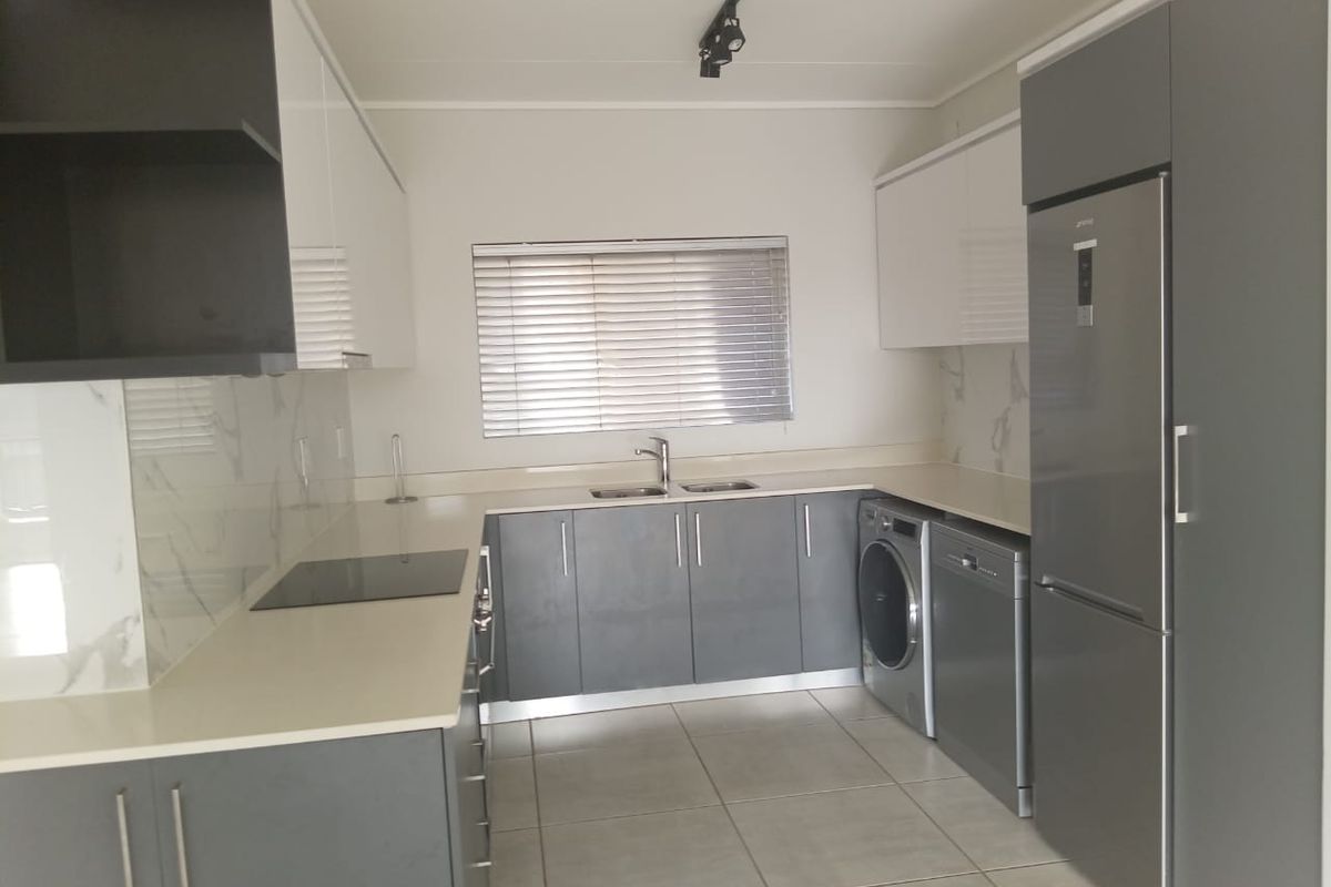 Modern kitchen featuring sleek grey and white cabinetry, stone countertops, marble-look splashbacks, and integrated appliances including a hob and fridge.