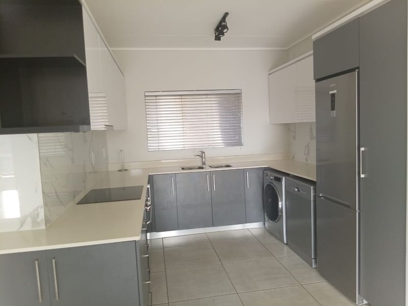 Modern kitchen featuring sleek grey and white cabinetry, stone countertops, marble-look splashbacks, and integrated appliances including a hob and fridge.