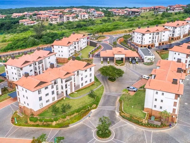 Aerial view of a modern residential apartment complex featuring landscaped grounds, paved internal roads, and a secure gated entrance near the coast.