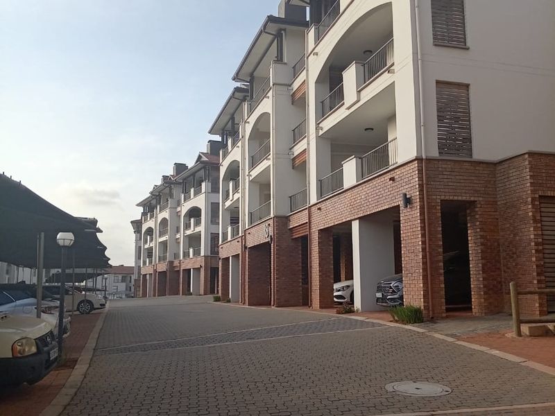 Exterior view of a multi-story apartment complex featuring brick and plaster facade, private balconies, and paved driveway with covered parking bays.