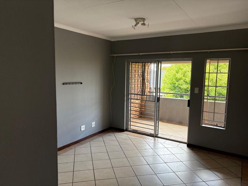 An empty living room featuring tiled flooring, grey walls, and a sliding glass door leading to a balcony with security gates.
