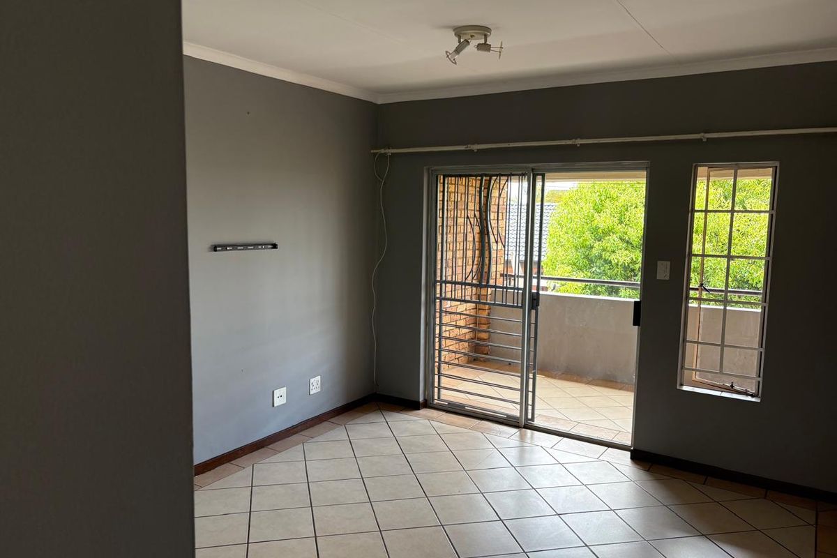 An empty living room featuring tiled flooring, grey walls, and a sliding glass door leading to a balcony with security gates.