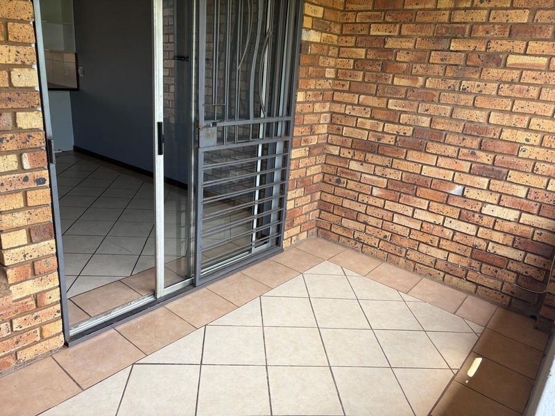 A covered patio area featuring exposed brick walls, tiled flooring, and a sliding glass door with a security gate.