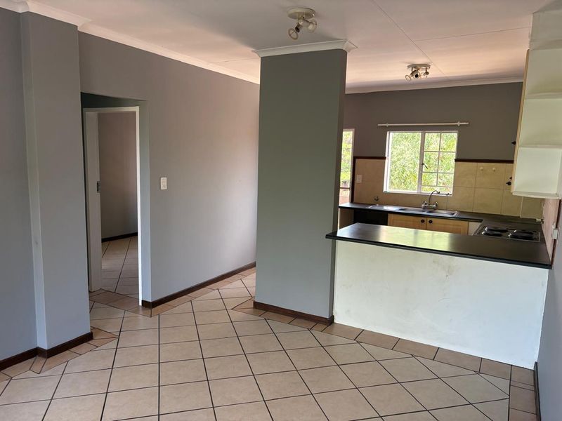 An open-plan living and kitchen area featuring tiled flooring, a breakfast counter, and built-in kitchen cabinetry with a hob and sink.