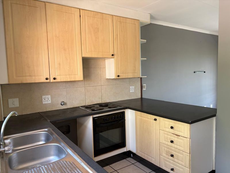 A functional kitchen featuring light wood-finish cabinetry, dark laminate countertops, a built-in oven with electric hob, and a double stainless steel sink.