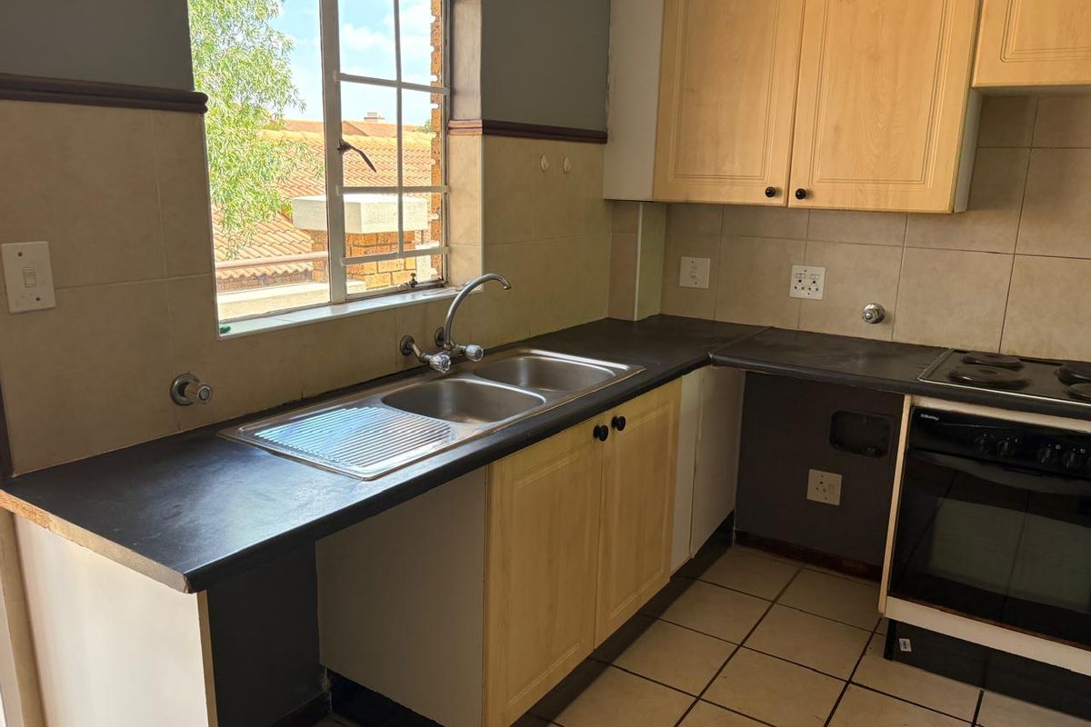 A functional kitchen featuring light wood cabinetry, dark countertops, a double sink, and a built-in electric oven with hob.